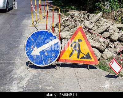 Road repair sign closeup. Road sign repair work. Roadwork warning signs on the roadside near a pile of concrete behind a barrier Stock Photo