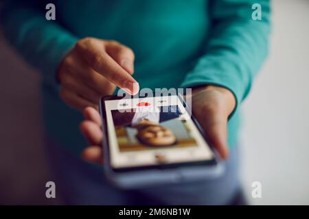 Mobile phone in hands of woman who scrolling through profiles of men and pressing red heart button. Stock Photo