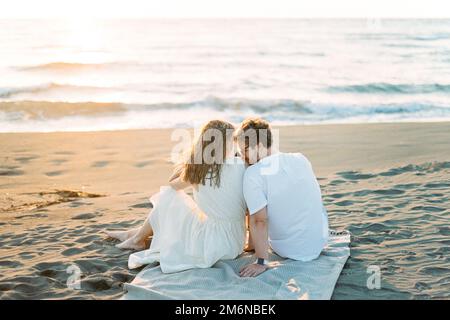 Man kissing woman shoulder while sitting on a blanket on the beach Stock Photo