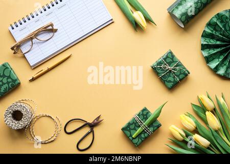 Weekly planner, female desktop. Spring freesia, tulip flowers and gift boxes. Orange, yellow, green, purple background with green wrapping paper Stock Photo