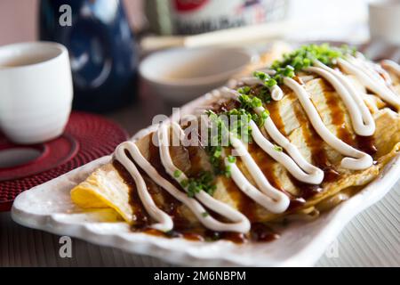 Japanese rice omelette stuffed with vegetables, meat and covered with various sauces. Stock Photo