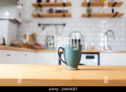 Green coffee cup on kitchen table blurred kitchen in background Stock Photo