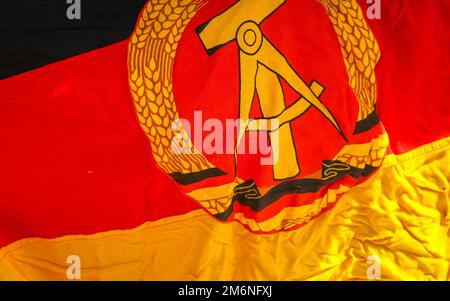 A piece of the flag of the former GDR with emblem, hammer, compass, ear wreath. Stock Photo