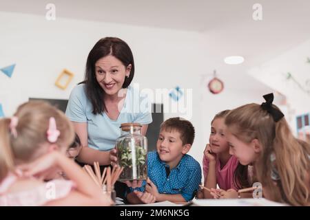 Female Teacher with kids in biology class at elementary school conducting biology or botanical scientific experiment about susta Stock Photo