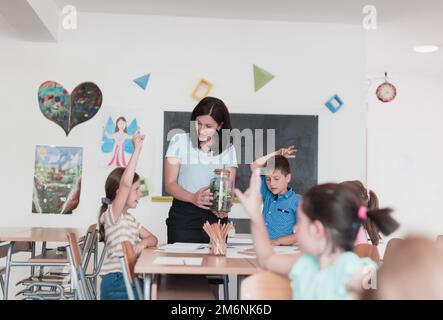 Female Teacher with kids in biology class at elementary school conducting biology or botanical scientific experiment about susta Stock Photo