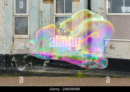Rainbow coloured giant soap bubble floating past a derelict building Stock Photo