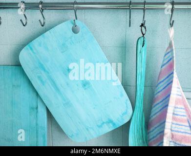 Wooden cutting boards, a cooking spatula, a kitchen towel hang on hooks in the kitchen, against the background of a tiled wall, Stock Photo