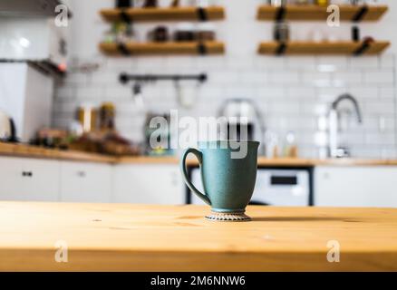 Green coffee cup on kitchen table blurred kitchen in background Stock Photo