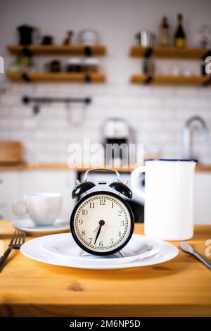 Intermittent fasting concept alarm clock on kitchen table Stock Photo