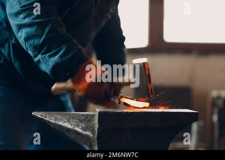 Blacksmith forges and makes metal detail with hammer and anvil at forge Stock Photo
