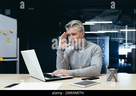 Senior thinking businessman working inside office with laptops, man thinking about important financial decision. Stock Photo