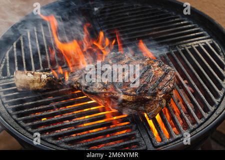 Barbecue dry aged wagyu tomahawk steak offered as close-up on a charcoal grill with fire and smoke Stock Photo