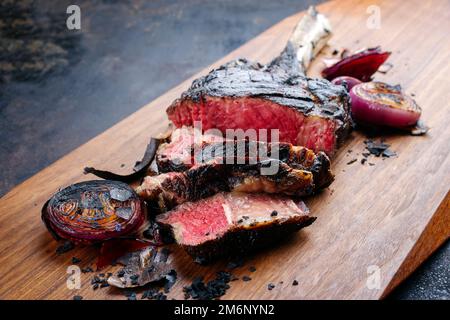 Traditional barbecue dry aged Kobe tomahawk steak with grilled onions served as close-up on a wooden design board Stock Photo