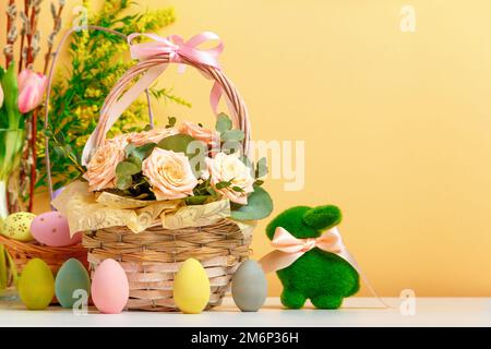 Easter still life. A basket with flowers and eggs, a toy rabbit on the table. copy space Stock Photo