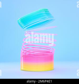 Rainbow slinky toy, spring and plastic product in studio isolated against a blue background mockup. Flexible toys, colorful spirals and childhood item Stock Photo