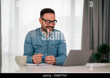 Happy caucasian office worker, attending a morning meeting at his desk, using laptop. Stock Photo
