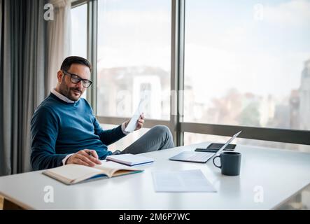 Calm, casual young adult businessman, checking his notes, making sure they match the numbers. Stock Photo