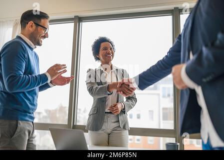 Smiling african american woman, handshaking with her colleague, while her male coworker claps. Stock Photo