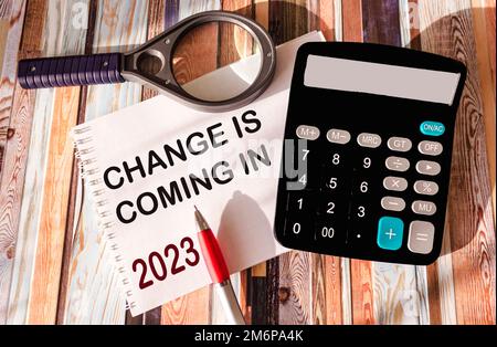 notepad with the word change is coming in 2023 on a vintage background with a magnifying glass, calculator and pen Stock Photo