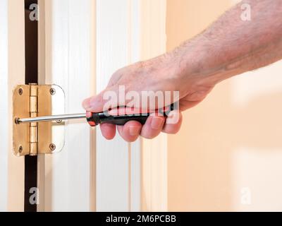 Male carpenter repairing door hardware. Handyman using screwdriver to install screw on door hinge. Stock Photo