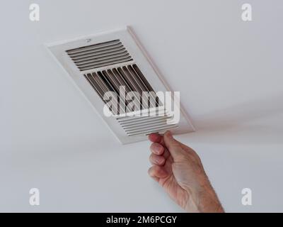Handyman adjusting HVAC ceiling air vent. Air flow adjustment for overhead home heat and air conditioning ventilation duct. Stock Photo