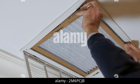 Man replacing dirty HVAC air filter in ceiling vent. Home air duct system maintenance for clean air. Stock Photo