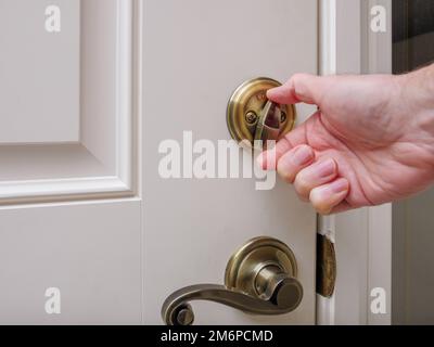 Close up of man locking deadbolt door lock on white entry door. Home security burglar and robbery prevention. Stock Photo