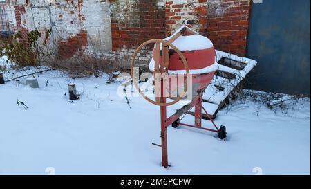 An old concrete mixer stands on a construction site in winter. Stock Photo