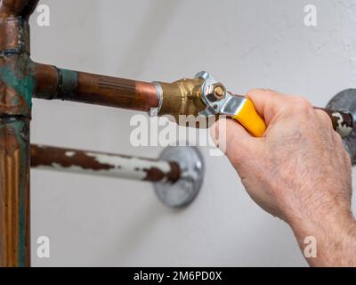 Plumber turning water shut off valve. Copper plumbing pipe with brass water supply valve and yellow stopcock handle. Stock Photo