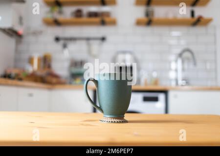 Green coffee cup on kitchen table blurred kitchen in background Stock Photo