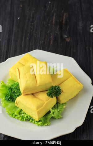 Tahu Susu Lembang, Fresh Made Raw Bean Curd Yellow Bandung Tofu on Black Wooden Table. Concept of Vegan Healthy Meal.  Copy Space for Advertisement, T Stock Photo