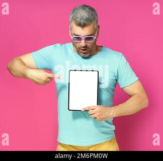 Pointing at digital tablet handsome man looking at white screen lowered his head wearing casual blue shirt and sunglasses isolat Stock Photo