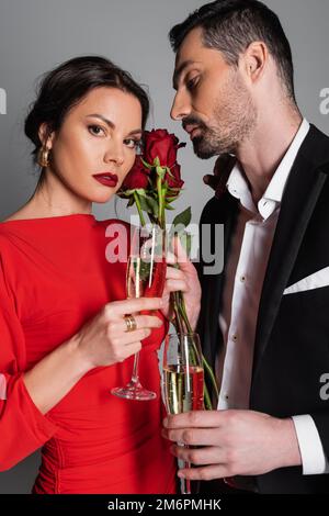 Elegant woman looking at camera near boyfriend with champagne and roses isolated on grey,stock image Stock Photo