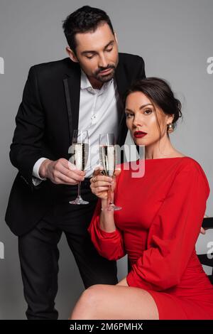 Elegant man in suit holding champagne while girlfriend in dress looking at camera on grey background,stock image Stock Photo