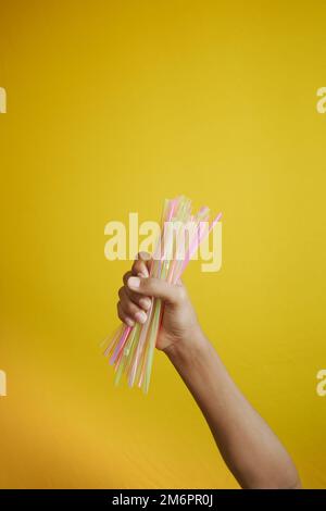 child hand holding many straw straws against yellow background  Stock Photo