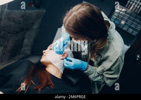 Young woman doing piercing at beauty studio salon. Stock Photo