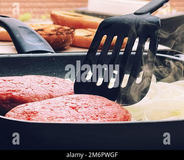 Cooking minced beef burger on cast iron grill skillet outdoors, red meat on frying pan, grilling food in the garden, English cou Stock Photo