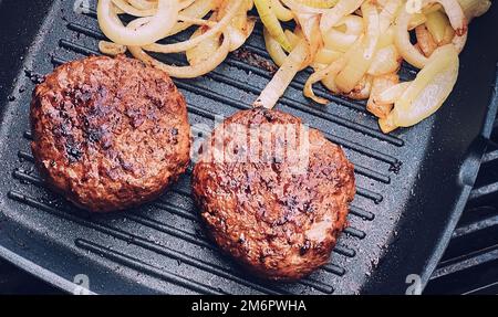 Cooking minced beef burger on cast iron grill skillet outdoors, red meat on frying pan, grilling food in the garden, English cou Stock Photo