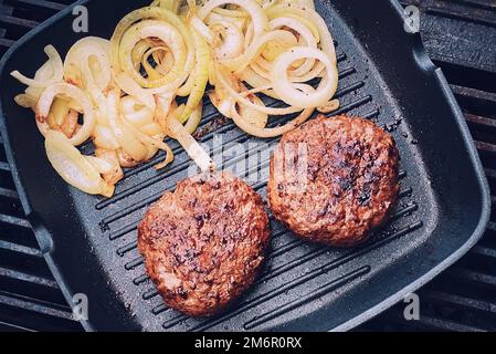 Cooking minced beef burger on cast iron grill skillet outdoors, red meat on frying pan, grilling food in the garden, English cou Stock Photo