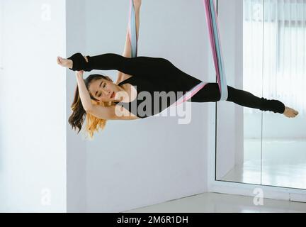 Young beautiful Asian dancer dressed in black color performing aerial dance with multi-color fabrics in the studio. Stock Photo