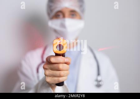 Healthcare worker holding gun thermometer and wearing coronavirus Covid19 mask Stock Photo