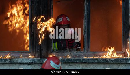 Firefighter hero carrying baby girl out from burning building area from fire incident. Rescue people from dangerous place Stock Photo