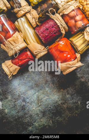 Closed pickling jars with various vegetables on stone table Stock Photo