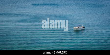 Lonely small holiday yacht moored in the ocean. Idyllic calm blue sea water Stock Photo