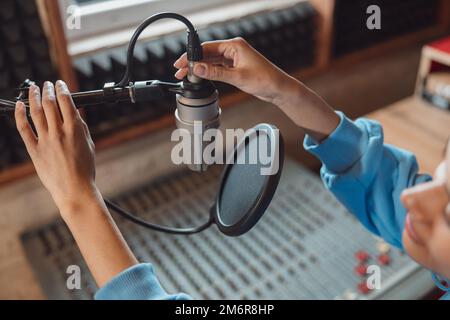 Close-up of audio engineer working in sound record studio, using microphone, mixing board, software to create new song Stock Photo