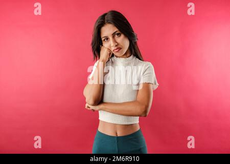 Portrait of young brunette woman wearing white ribbed crop isolated over red background very bored and waits with head resting on the fist. It is so b Stock Photo