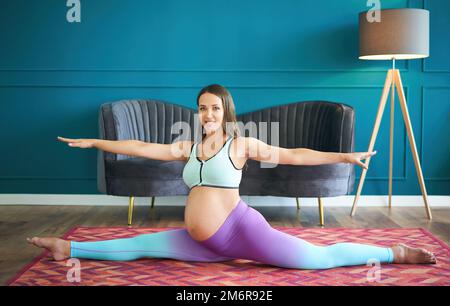 Pregnant sporty woman practicing yoga at home doing stretching exercise the side split pose Stock Photo