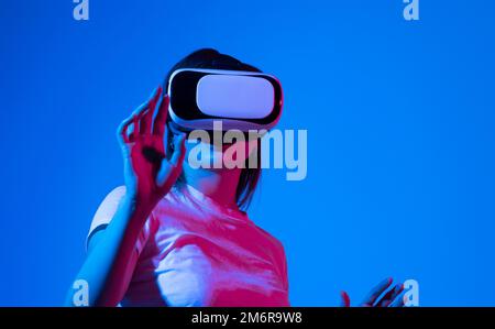 Woman in white shirt wearing VR glassess, VR set equipment for exploring a metaverse. Girl wearing a VR headset and interacting with virtual reality Stock Photo