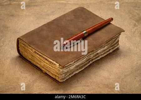 retro leather-bound journal with decked edge handmade paper pages and a stylish pen on a textured bark paper, journaling concept Stock Photo