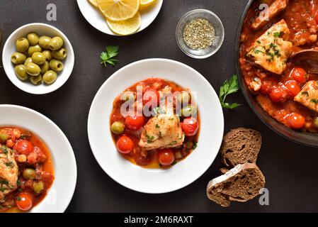 Cod stew with chickpeas, cherry tomatoes and olives over dark stone background. Top view, flat lay Stock Photo